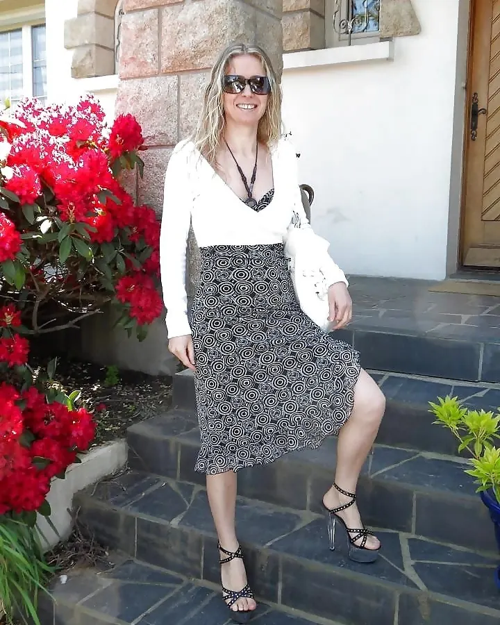 Femme plus âgée aux cheveux blonds assise sur un canapé, vêtue d'un haut turquoise et d'un short rouge.