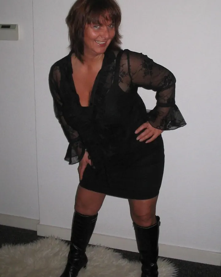 Femme aux cheveux bruns noirs, portant une robe noire en dentelle et des bottes noires, debout sur une fourrure blanche.