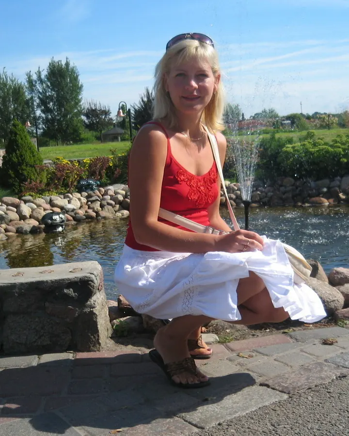 Femme blonde en robe rouge, accroupie près d'un bassin