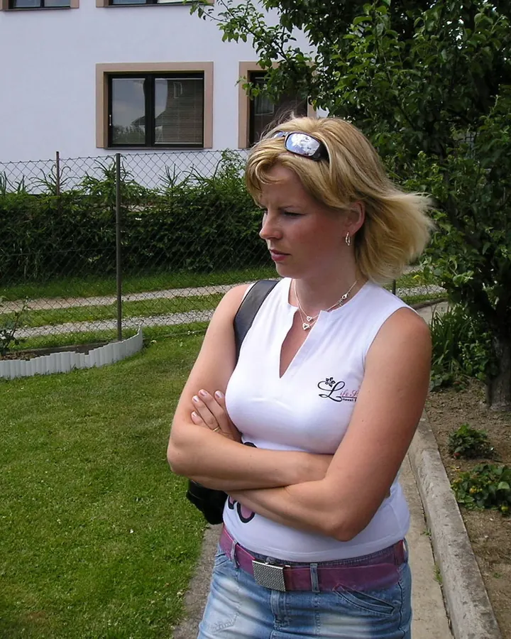 Femme blonde en haut blanc et jeans debout dans un jardin avec les bras croisés