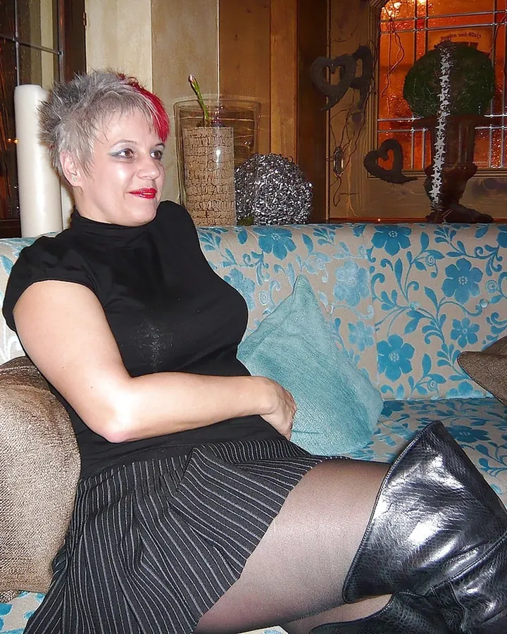 Femme aux cheveux blonds, en lingerie noire, allongée sur un lit, les jambes croisées, dans une chambre aux tons sombres.