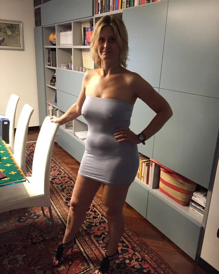 Femme aux cheveux blonds, en haut noir, posant dans une chambre.