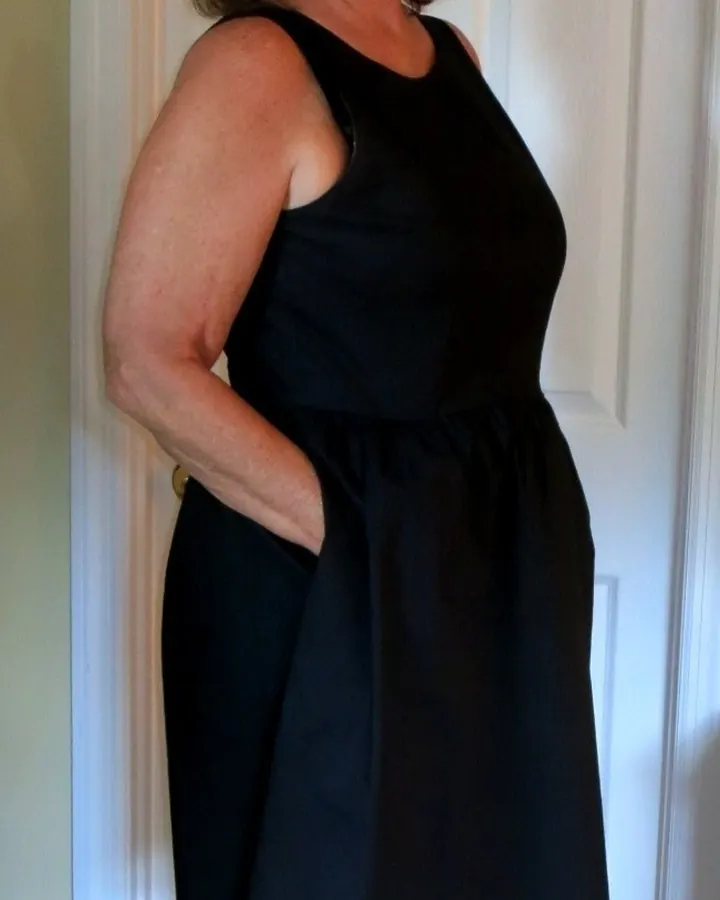 Femme aux cheveux bruns, en robe noire, debout devant une porte blanche